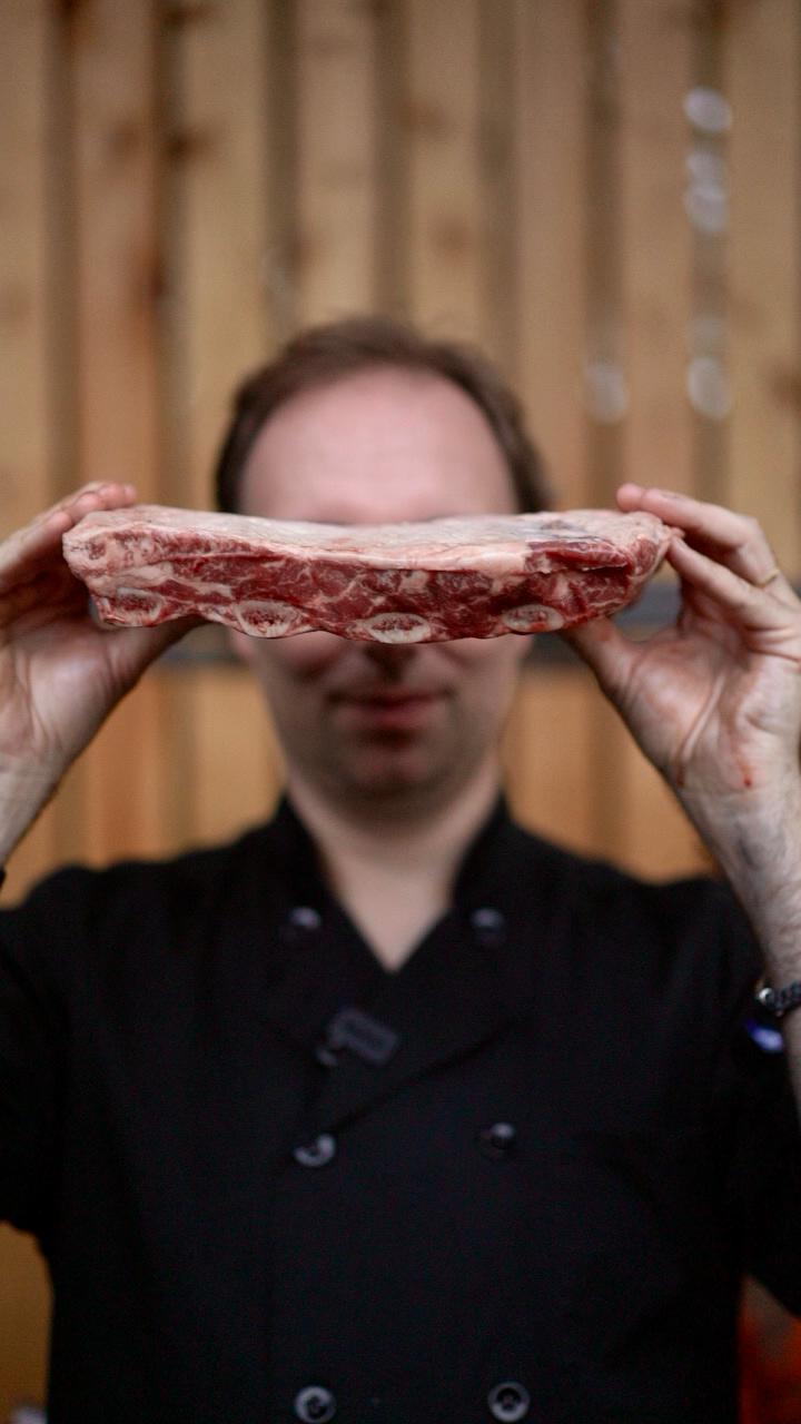 Person holding a piece of raw meat in front of their face with a wooden background